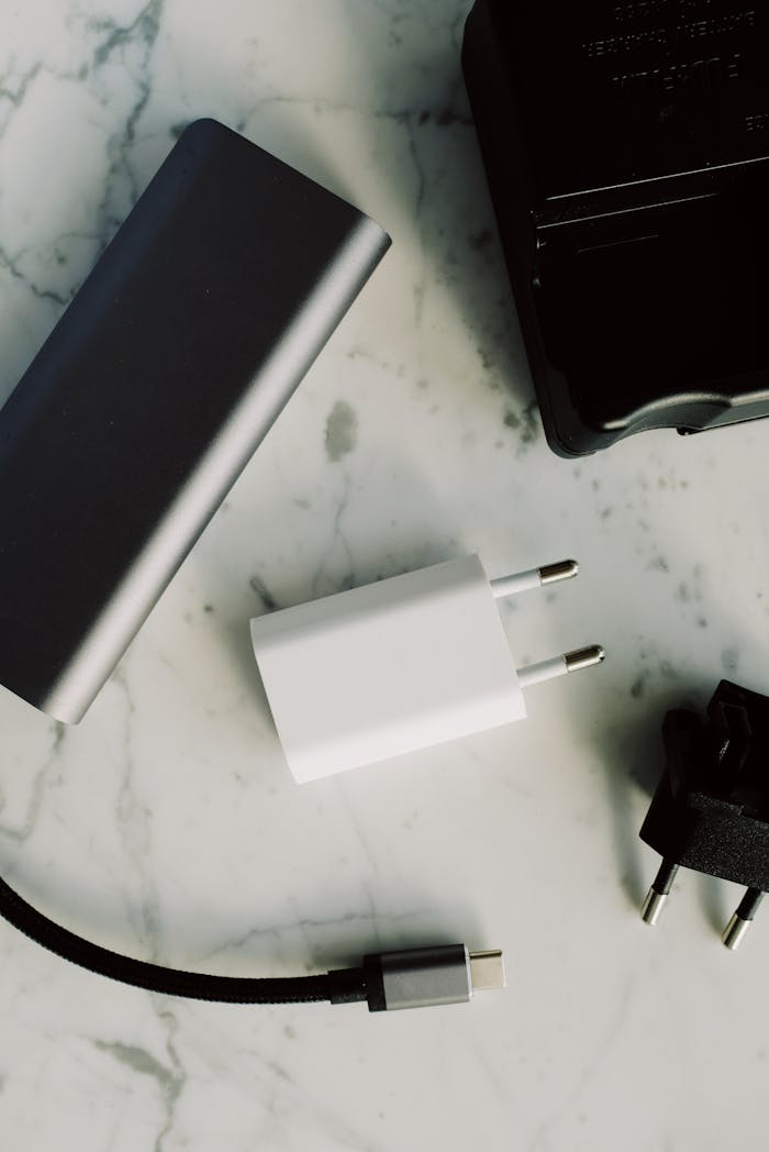 Composition of various modern charging units with adapter and small black external battery pack with short cable placed on white marble table